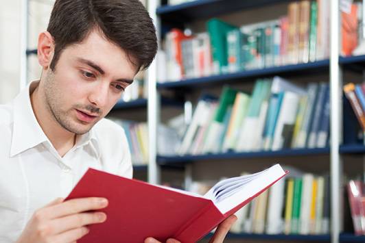Quelle: AdobeStock_69291962 Interessiert lesender junger Mann vor einem Bücherregal.