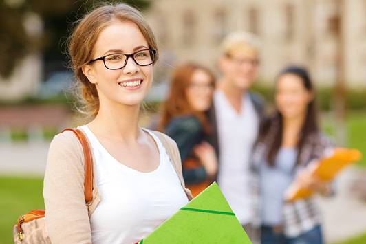 Quelle: AdobeStock_59063897_Syda Productions Studentin schaut lachend zum Fotografen. Im Hintergrund Gruppe mit drei Studierende.