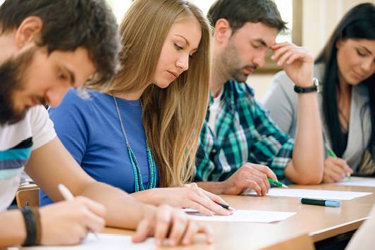 Quelle: AdobeStock_54871954 Eine Studentin sitzt zwischen drei Studierenden: Alle konzentrieren sich auf vor sich liegende Dokumente.